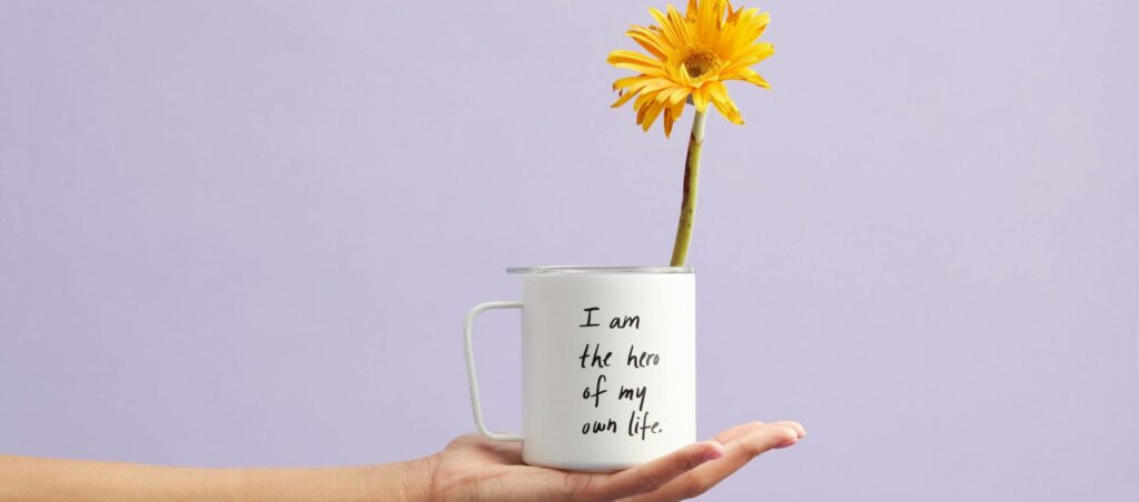 Hand holding a mug with a sunflower and motivational quote, set against a purple background.