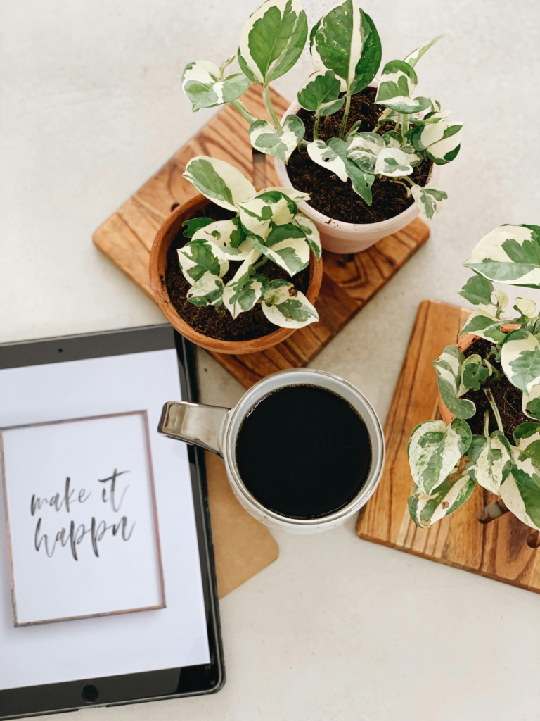 Modern workspace setup featuring a black coffee, tablet, and potted plants for inspiration.